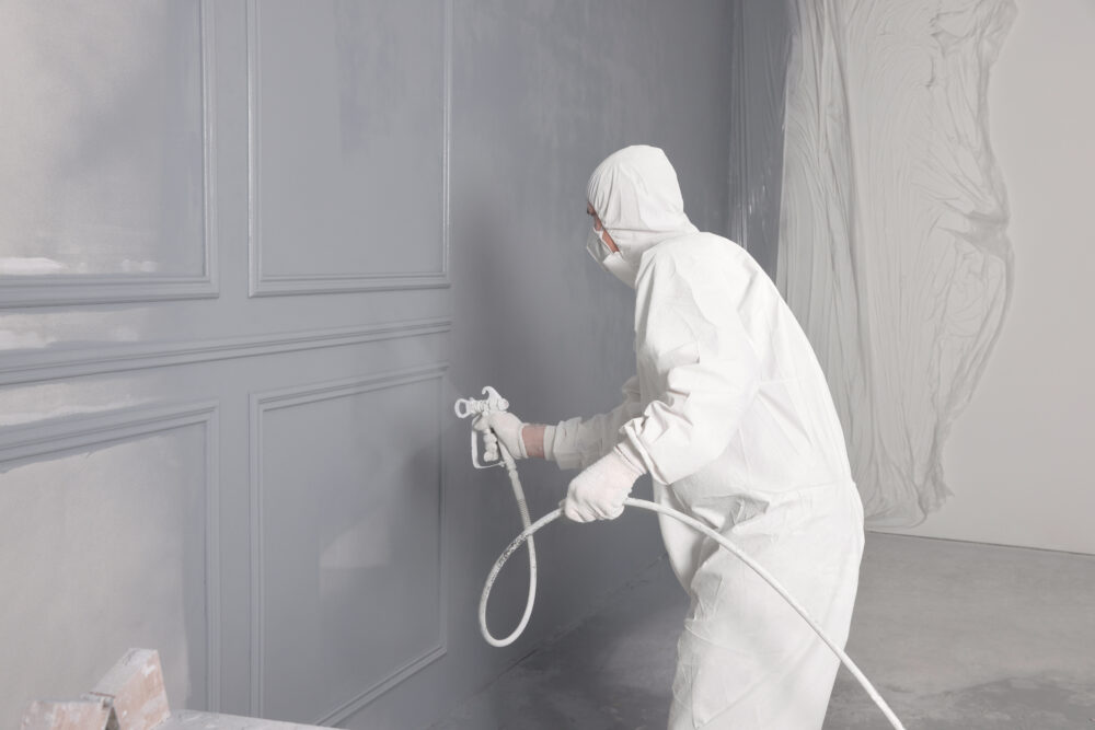 Decorator dyeing wall in grey color with spray paint indoors